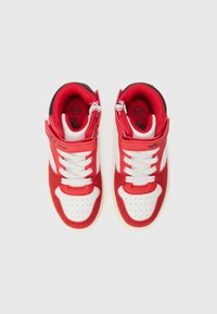 Baskets de sport rouges et blanches avec un matériau en daim et synthétique, col rembourré, lacets plats et design de bout perforé. Sangle ajustable incluse.