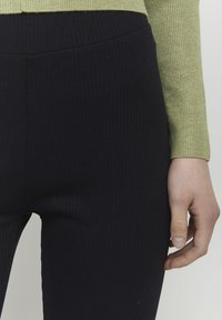 Csíkozott, magas derékú fekete leggings egy texturált, hosszú ujjú világoszöld toppal párosítva, fókuszálva az ujjakra és a derékpántra.