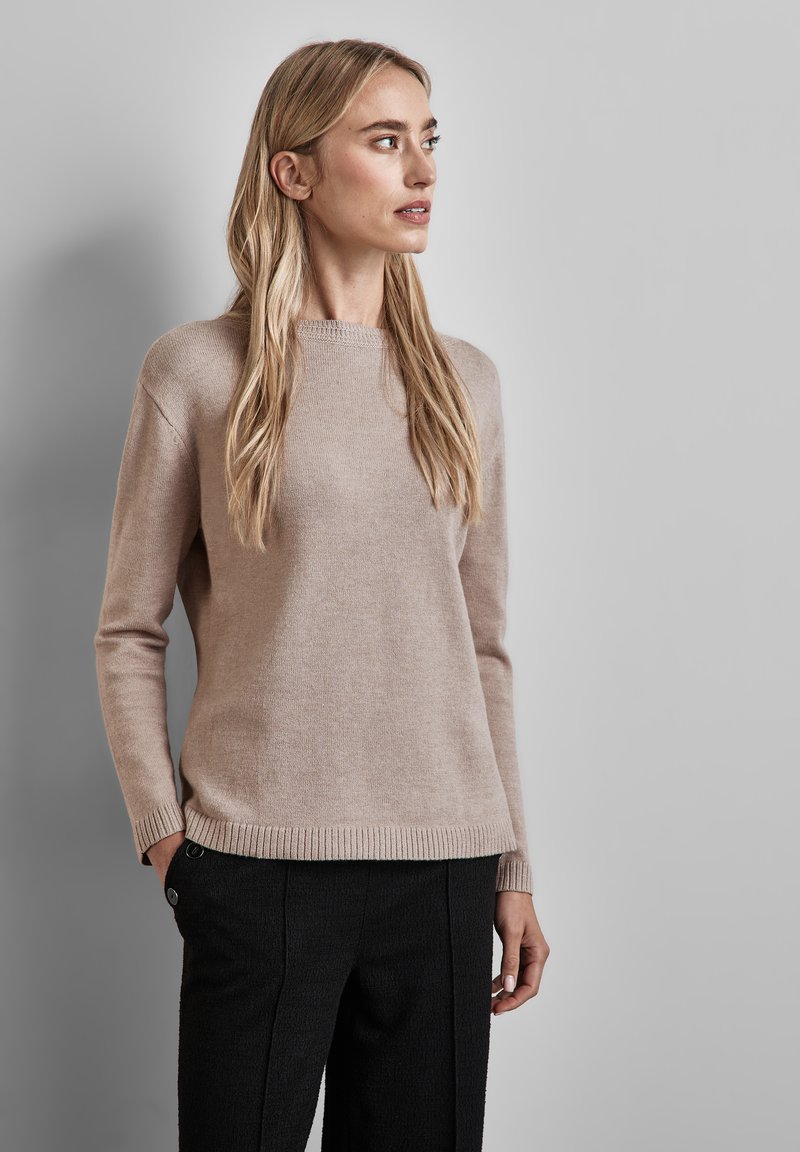 Beige Strickpullover mit langen Ärmeln und Rundhalsausschnitt, mit gerippten Bündchen und Saum. Getragen mit strukturierten schwarzen Hosen.