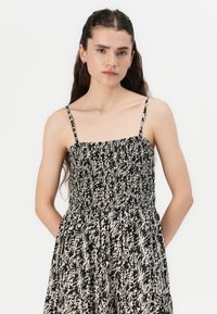 Rochie cu imprimeu floral în nuanțe de negru și crem, cu un corset elastic și bretele subțiri, având un design de fustă lejeră și vaporoasă.