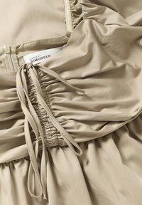 Robe beige avec texture froncée, liens ajustables et fermeture éclair dissimulée. Étiquette indiquant "Karen by Simonsen." Tissu doux et lisse.