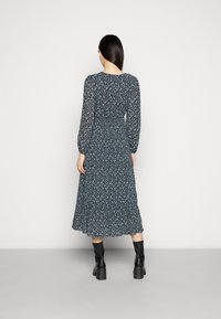 Robe à manches longues, motif floral en bleu foncé avec une taille cintrée, une jupe évasée et un ourlet festonné, associée à des bottes noires jusqu'aux genoux.