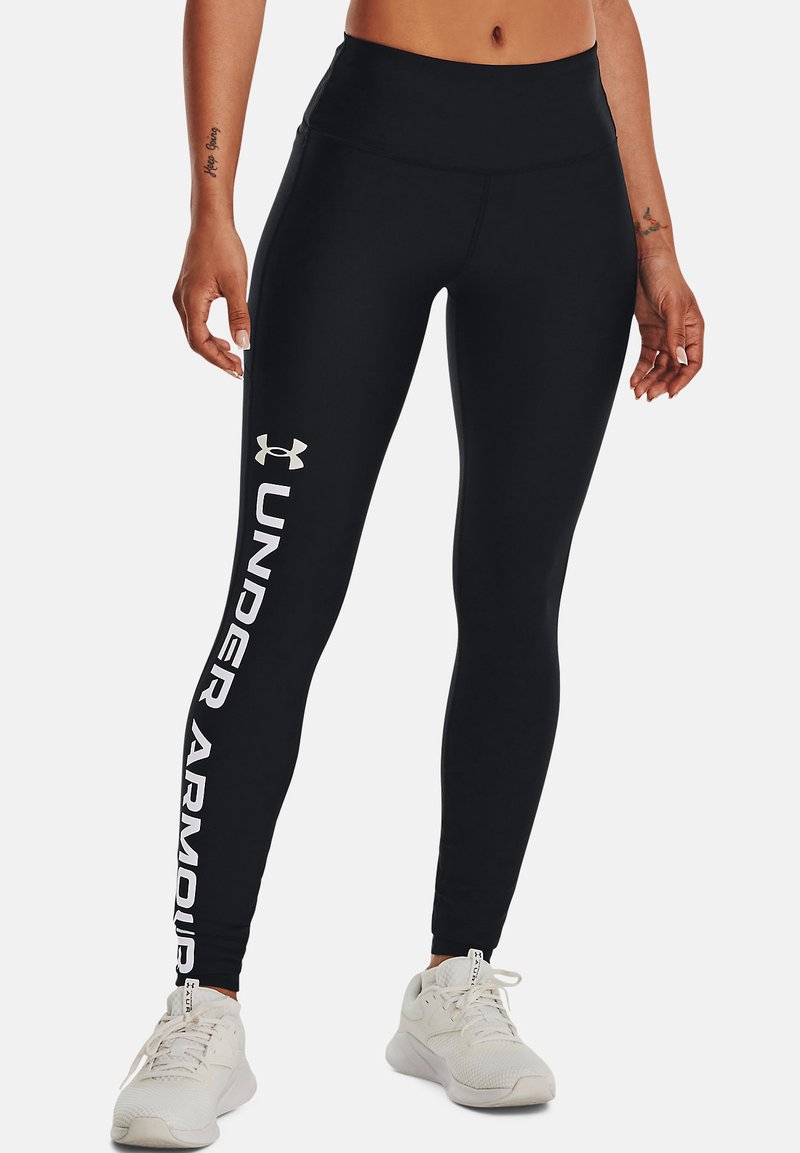 Leggings noirs en matériau extensible avec une taille haute. Présente le texte et le logo blanc "UNDER ARMOUR" le long de la jambe gauche.