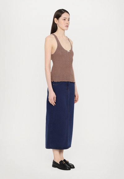 Canottiera a righe marrone con orlo scallop, abbinata a una lunga gonna di jeans blu scuro. Il modello indossa mocassini neri con un accento oro.