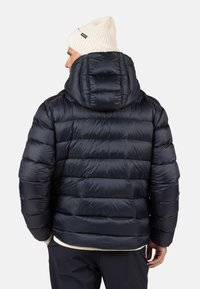 Giacca puffer blu navy con design trapuntato e cappuccio, caratterizzata da una texture liscia e lucida. Include un berretto lavorato a maglia color crema.