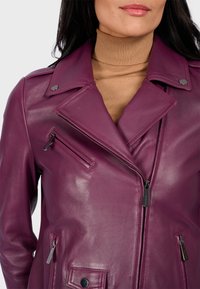 Fialová kožená motocyklová bunda s zipovým zapínáním, cvokovými detaily na límci a několika kapsami s hladkou texturou.