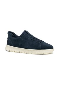 Zapatilla de ante azul marino con punta redonda, parte superior con cordones y una suela blanca flexible que presenta ranuras curvas para mayor tracción.
