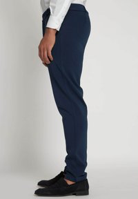 Mørkeblå bukser med slim fit, lavet af et glat stof. Har flad front og sidelommer, parret med sorte ruskind loafers.