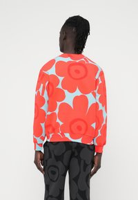 Κόκκινο φούτερ με λουλουδάτο μοτίβο και ανοιχτό μπλε φόντο, με ριμπ μανσέτες και τελείωμα, συνδυασμένο με μαύρο παντελόνι με μοτίβο.