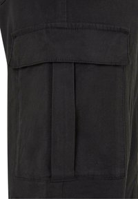 Tessuto nero dei pantaloni cargo con una finitura testurizzata, caratterizzato da un grande pattina della tasca e dettagli di pieghe laterali. Costruzione della vita standard.