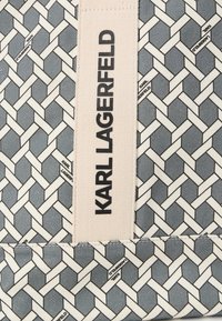 Szürke mintás szövet, amelybe egy egymásba szőtt mintázat van belefonva. Egy krémszínű címke látható, rajta a "KARL LAGERFELD" logo jól láthatóan.