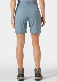 Vaaleansiniset polvipituudet shortsit, joissa on joustava vyötärönauha. Yhdistetty harmaisiin vaelluskengiin, joissa on kestävä pohja ja hengittävät verkkokankaiset paneelit.