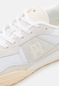 Sneakers bianchi con una tomaia in rete testurizzata, sovrapposizioni in suede e suola beige. Logo embossato sul lato e etichetta con marchio sul tallone.