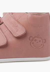 Scarpa in pelle rosa con due cinturini in velcro, suola bianca e logo di una scimmia embossato sul lato. Texture liscia con dettagli di cucitura discreti.