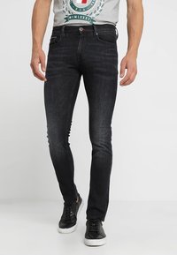 Vaqueros negros ajustados de denim, con un clásico diseño de cinco bolsillos, un ligero desgaste en la parte delantera y detalles cosidos en los bolsillos.