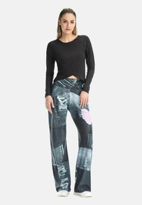 Schwarzes langärmeliges Oberteil mit kurzem Schnitt und rundem Ausschnitt, kombiniert mit weitem, patchwork Jeanshosen mit abgenutzten Texturen und verschiedenen Farben.