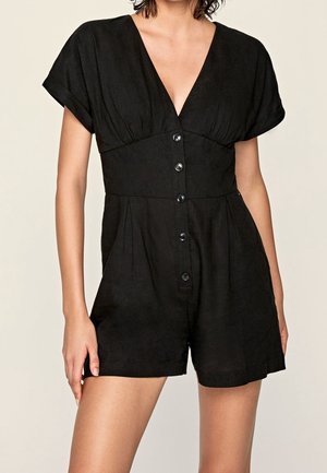 Vrouw draagt een zwarte korte mouwen romper met knopen, V-hals en geplooide taille detail.