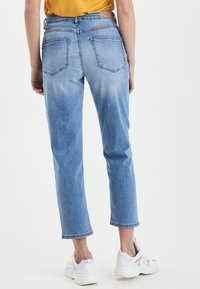 Light blue denim jeans with a straight cut, featuring two back pockets, faded texture, and rolled cuffs above white sneakers.