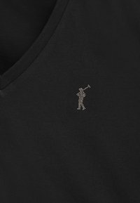 Svart v-ringad tröja i mjukt tyg med en liten, texturerad silverlogo föreställande en golfspelare på vänster sida.