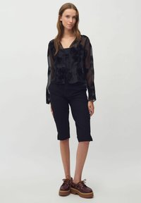 Bluza neagră semitransparentă cu broderie florală, asortată cu pantaloni negri până la genunchi și pantofi cu platformă maro, cu șireturi și talpă groasă.