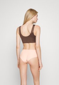 Brown cotton sports bra with wide straps paired with light pink seamless hipster briefs featuring a scalloped edge design.