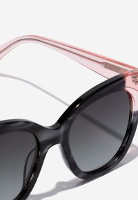 Ochelari de soare cu un gradient negru, cu un finisaj neted, având brațe transparente roz și o formă clasică supradimensionată.