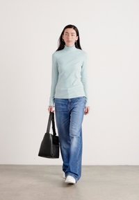Lichtblauwe coltrui, losse blauwe jeans, witte sneakers en een zwarte handtas. Minimalistisch ontwerp met koude texturen en moderne silhouetten.