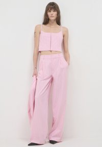 Rosa gestreiftes Crop-Top mit Spaghetti-Trägern und vorderen Knöpfen, kombiniert mit weit geschnittenen rosa gestreiften Hosen mit Seitentaschen. Glatte Textur.