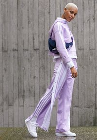 Tuta in lavanda con strisce laterali bianche, felpa con cappuccio e pantaloni con bottoni a pressione. Abbinato a scarpe bianche e una borsa blu navy. Texture liscia.