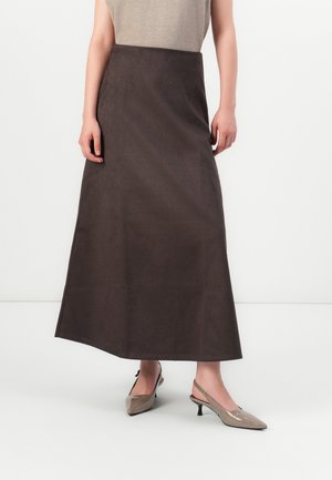 Kvinne med en høy midje, mørkebrun, ankellang skjørt og taupe pekede slingback hæler på hvit bakgrunn.