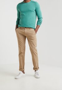 Turkos långärmad tröja med ribbade manschetter, kombinerad med tanfärgade chinos. Vita sneakers med platta sulor. Enkla och sl äta texturer genomgående.