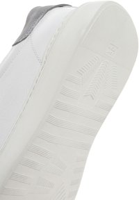 Sneaker en cuir blanc avec un talon en suède gris. La semelle en caoutchouc arbore un design de grip texturé et à motifs.