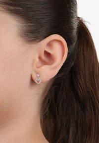 Pendientes de plata con un diseño circular y un motivo de corona, acentuados por una pequeña gema rosa encima de la pieza principal.