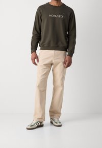 Olivgrön sweatshirt med texten "MORATO", beige byxor och olivgröna och gräddfärgade sneakers med bruna accenter. Avslappnad, löst sittande stil.