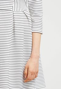 Randig klänning i svart och vitt med trekvartslånga ärmar, en figursydd bodice och en utsvängd kjol med subtila veck på sidan.