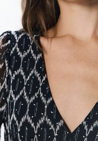 Robe noire à motifs avec un décolleté en V profond, en tissu texturé et des accents irisés en motif zigzag sur le corsage.