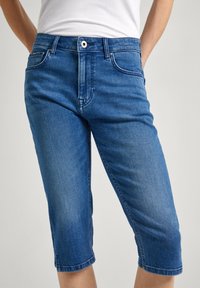 Džínové šortky ve středním odstínu s přímým střihem, vybavené předními kapsami, zapínáním na knoflík a ohrnovacími lemy.