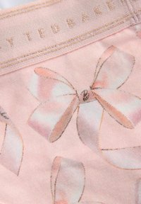 Leggings roses en tissu doux et texturé, ornés d'un motif de petits nœuds roses clairs et d'une taille brodée en or avec la marque "Ted Baker".