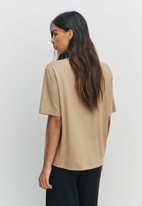 Luźna beżowa bluzka z krótkim rękawem, wykonana z miękkiego materiału. Posiada okrągły dekolt i prosty dół, w połączeniu z luźnymi czarnymi spodniami.