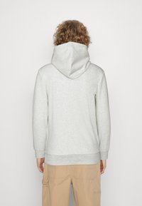 Grå hoodie med en stor, rund hætte, blød tekstur, og ribbede manchetter og kant. Båret med lysebeige cargo bukser.