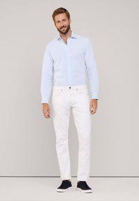 Camisa de botones azul claro, jeans blancos ajustados, zapatillas negras. Tela suave y corte entallado, con piernas de pantalón con puños y colores en contraste.