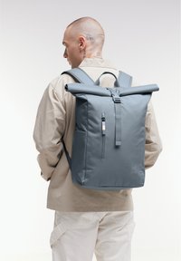 Gray roll-top backpack with adjustable straps, front zip pocket, durable material, featuring a subtle logo and sleek design.