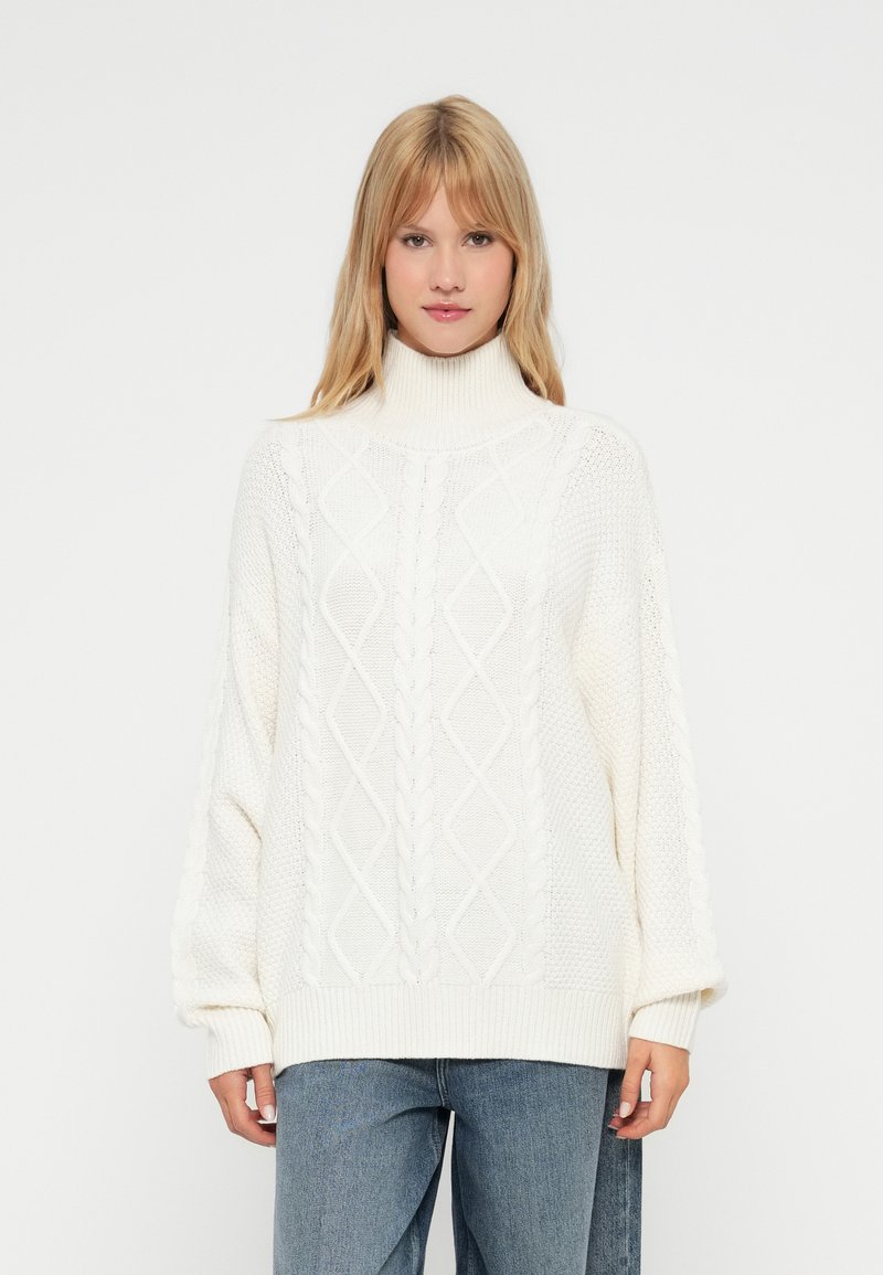 Pulover alb tricotat cu guler înalt tip turtleneck, având modele cu torsade și cusături deschise. Textură moale și croială supradimensionată.