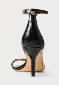 Μαύρη δερμάτινη ψηλοτάκουνη σαγιονάρα, με υφή από κροκόδειλο, λουράκι στον αστράγαλο με χρυσή λεπτομέρεια λογοτύπου και λεπτό τακούνι.