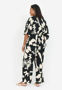 Tenue noire et écrue à motifs floraux avec une coupe ample et décontractée. Le haut présente des manches courtes et une taille élastique ; pantalons à jambes larges.