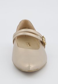 Bailarinas en un acabado metálico beige claro con punta redondeada, que presentan una sola correa con herrajes dorados. Textura suave.