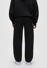 Sort oversized sweatshirt med tekstureret branding på ryggen, parret med matchende sorte sweatpants og hvide sneakers. Glat stof, afslappet pasform.
