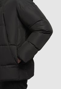 Sort pufferjakke med en quilted design, overdreven krave og et tekstureret stof med et logo accent på ærmet.