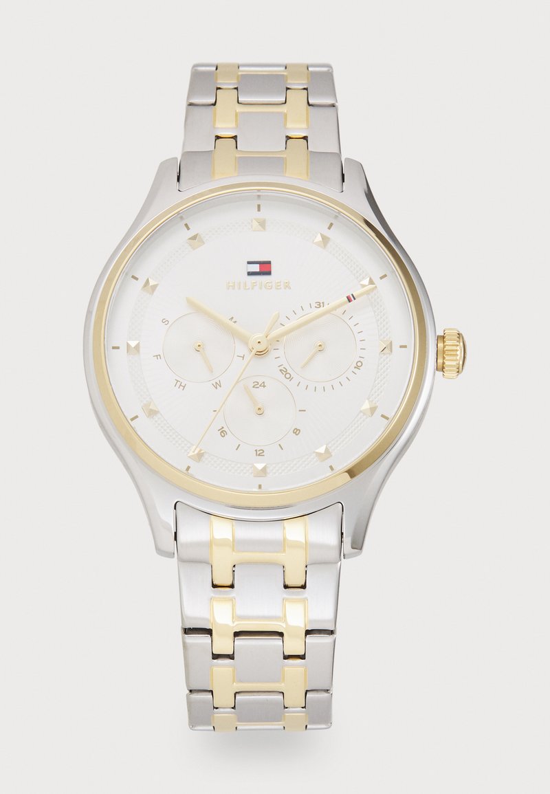 Ezüst és arany színű fém karóra fehér számlappal, három kisméretű számlap, arany órák jelzői és textúrázott felület jellemzi.