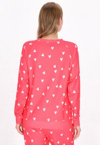 Roze sweatshirt van zacht materiaal met witte hartpatronen, voorzien van een ronde halslijn, lange mouwen en geribde manchetten en een zoom.